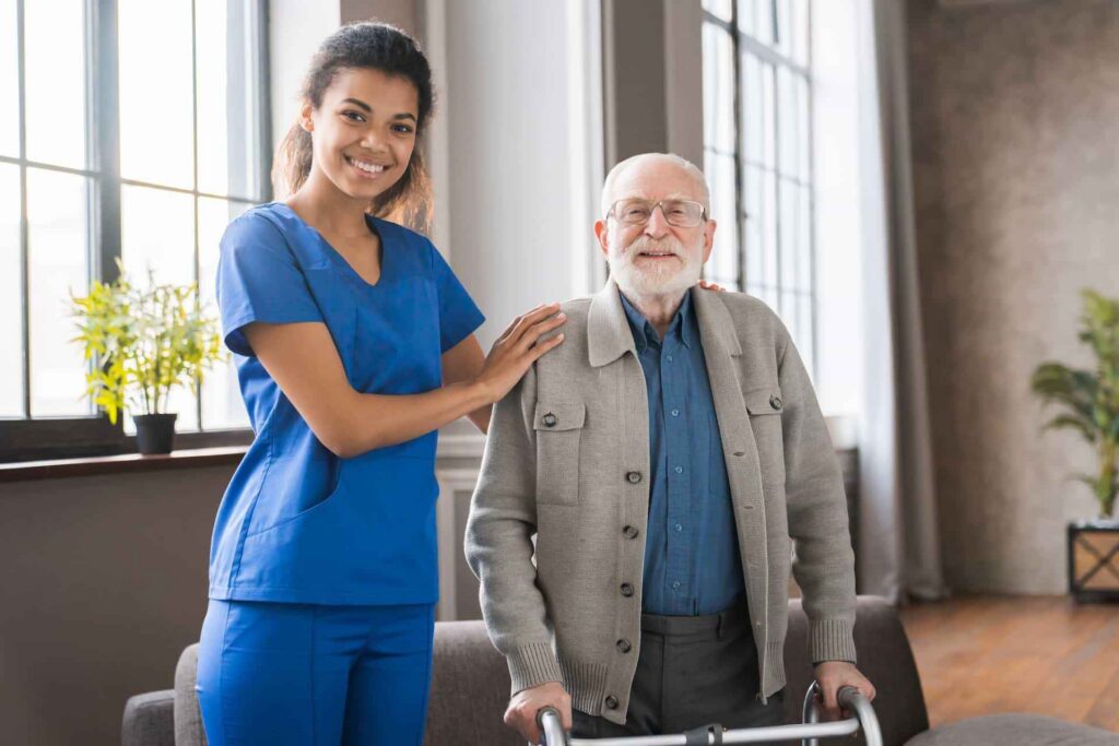 Home health aide assisting an elderly man with mobility support inside a home